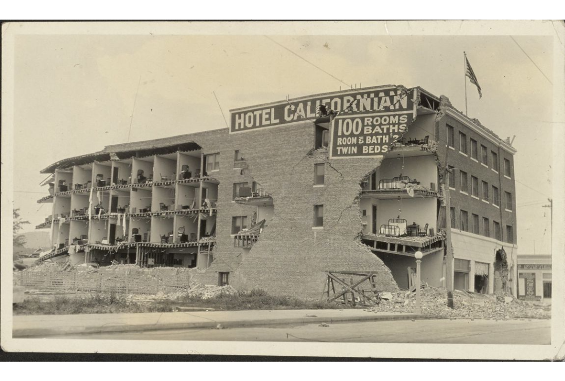 Damaged Hotel Californian building with exposed rooms and debris, a partially cut off sign on the building reads "100 Rooms Baths Room & Baths Twin Beds".